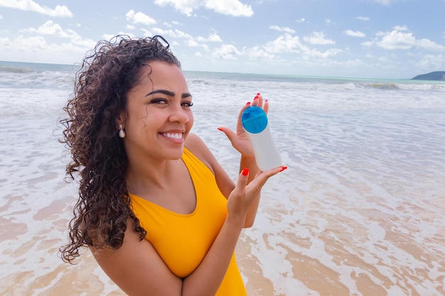 Piękna młoda kobieta na plaży szczęśliwa trzymająca w dłoniach krem z filtrem przeciwsłonecznym Letnia koncepcja pielęgnacji skóry Kobieta pokazująca krem przeciwsłoneczny na plaży