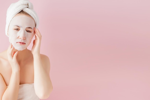 Zdjęcie piękna młoda kobieta nakłada kosmetyczną maskę tkanki na twarz na różowym tle koncepcja leczenia i technologii opieki zdrowotnej i urody