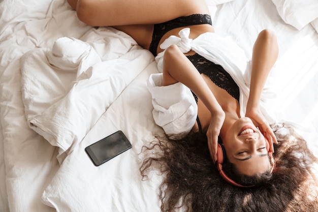 Piękna Młoda Kobieta Nosi Słuchawki Leżąc Na łóżku Ze Smartfonem W Domu