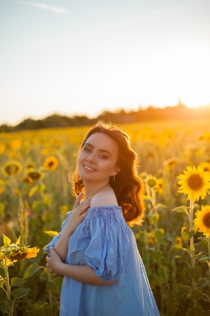 Piękna młoda kobieta o ciemnych kręconych włosach w polu słonecznika Model w stylowej niebieskiej sukience Summer Warmly