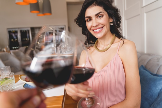 Piękna młoda kobieta patrząca i uśmiechająca się, stukając się szklankami napoju alkoholowego z mężczyzną
