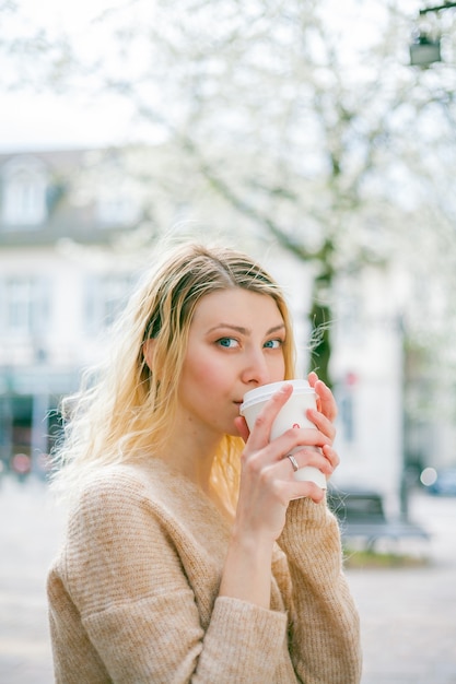 Piękna młoda kobieta pije kawę, aby przejść na ulicę europejskiego miasta