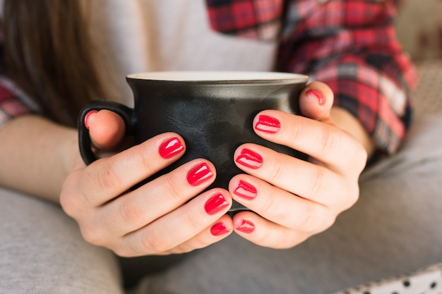 Piękna młoda kobieta pije kawę cappuccino, doskonały manicure czerwony żelowy lakier.