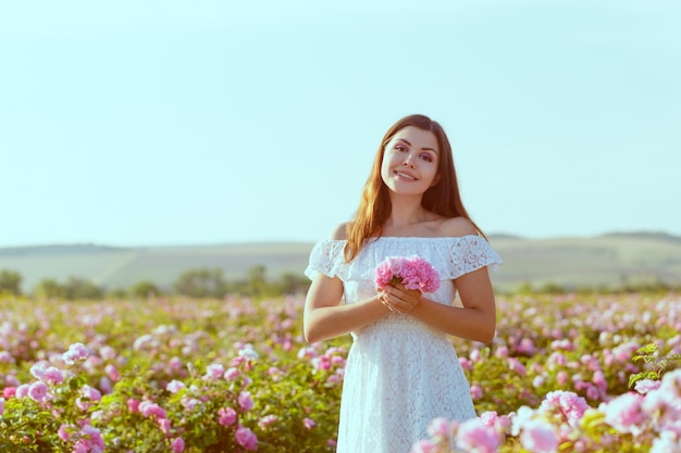 Piękna młoda kobieta pozuje blisko róż w ogródzie.