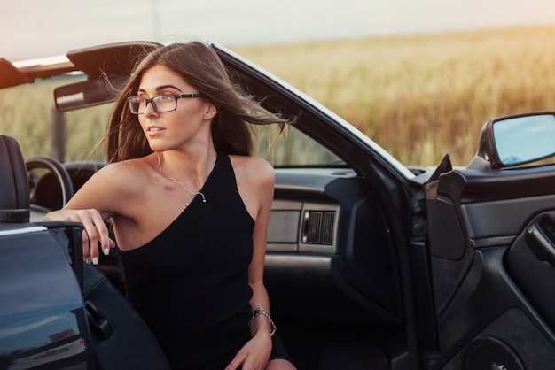 Piękna młoda kobieta pozuje blisko samochodu na drodze