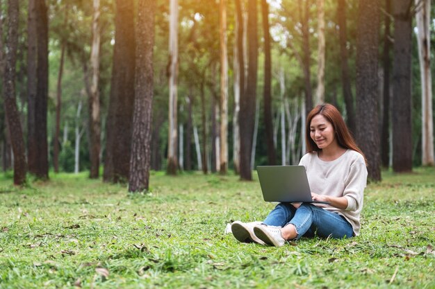 Piękna młoda kobieta pracuje i pisze na klawiaturze laptopa, siedząc w parku