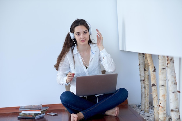piękna młoda kobieta relaksuje się i pracuje na laptopie nowoczesne biuro domowe podczas słuchania muzyki na białych słuchawkach