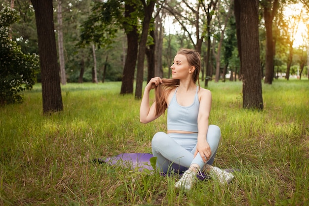 Piękna młoda kobieta robi joga w parku na trawie. Mata gimnastyczna, sprzęt sportowy. Trening na świeżym powietrzu. Zdrowy styl życia, odchudzanie, fitness. Wyszkolone muskularne ciało. Świeże powietrze. portret