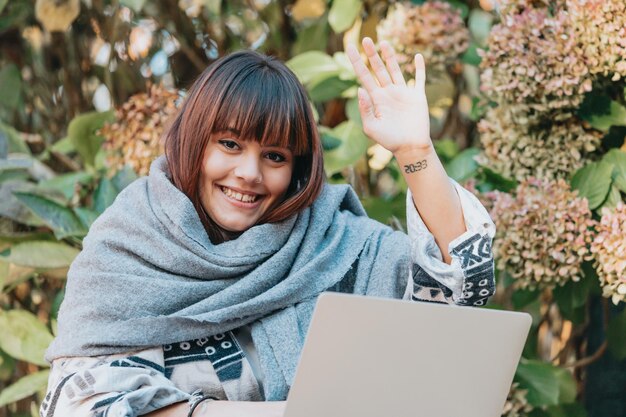 Piękna młoda kobieta siedzi na ławce w parku i pracuje na laptopie podczas zabawy