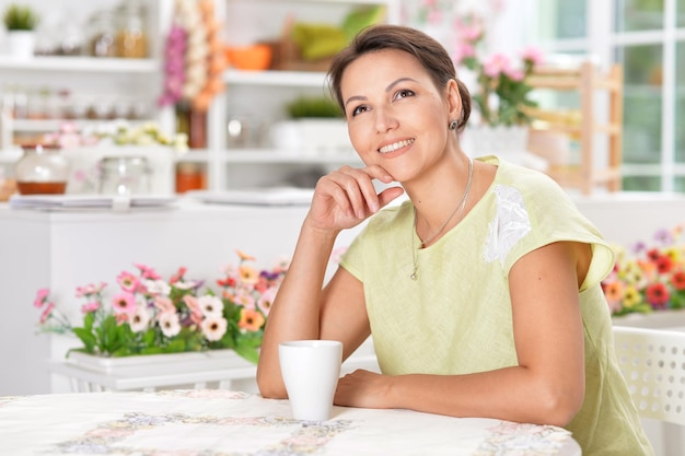 Piękna młoda kobieta siedzi przy kuchennym stole z filiżanką herbaty
