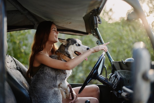 Piękna młoda kobieta siedzi za kierownicą swojego samochodu wraz z psem rasy husky i uśmiecha się radośnie, cieszy się podróżą