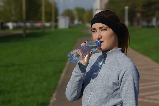 Piękna młoda kobieta trzyma butelkę wody po treningu w parku.