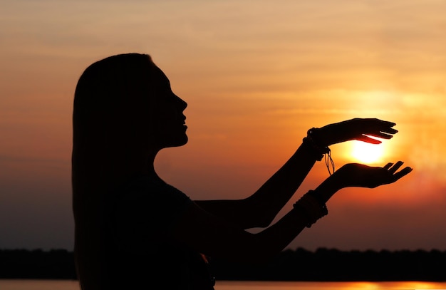 Piękna młoda kobieta trzyma słońce w dłoniach na sylwetce słońca