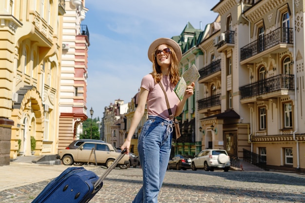 Piękna młoda kobieta turysta Przyjemny z mapą miasta i walizką w centrum miasta.