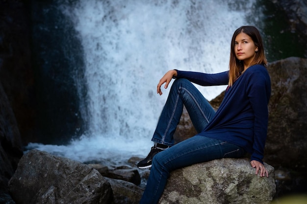 Piękna młoda kobieta turysta siedząca w pobliżu wodospadu
