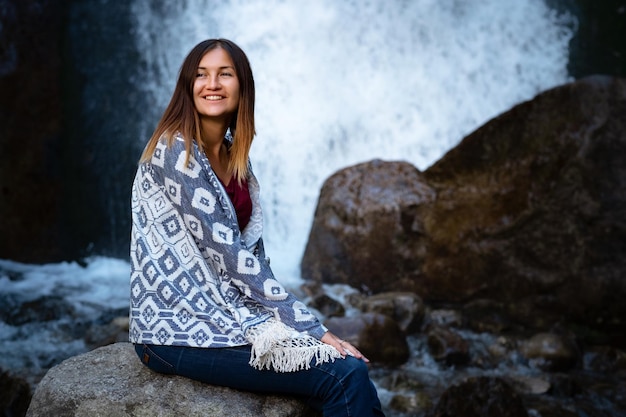 Piękna młoda kobieta turysta siedząca w pobliżu wodospadu