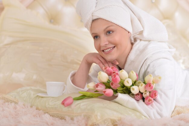 Piękna młoda kobieta ubrana w biały szlafrok i pijąca herbatę w domu