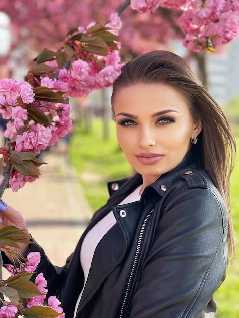 Piękna młoda kobieta ubrana w czarną kurtkę stoi w kolorze kwiatów sakury na wiosnę