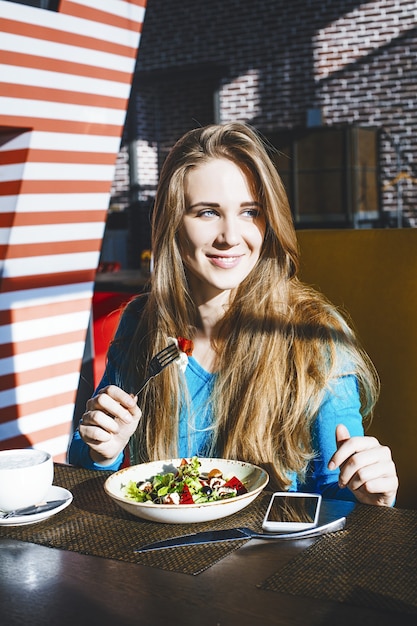 Piękna młoda kobieta udany modny i piękny telefon komórkowy i miskę sałatki w restauracji