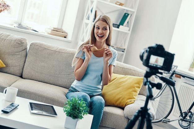 Zdjęcie piękna młoda kobieta uśmiecha się i pokazuje końcówki włosów podczas nagrywania filmów w mediach społecznościowych w domu