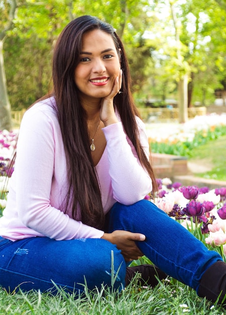Piękna młoda kobieta uśmiecha się i siedzi w parku miejskim z fioletowymi tulipanami