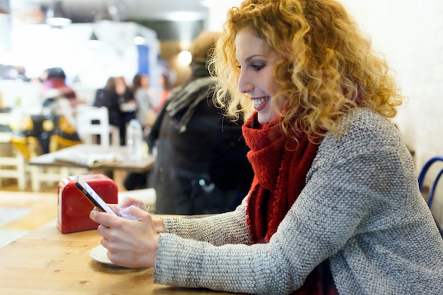 Piękna młoda kobieta używa jej telefon komórkowego przy kawiarnia sklepem.