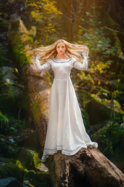 Piękna młoda kobieta w białej sukni pośrodku lasu