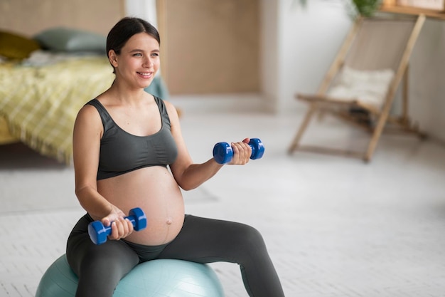 Piękna młoda kobieta w ciąży siedzi na fitball i trening z hantlami