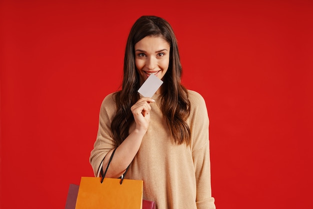 Piękna młoda kobieta w codziennej odzieży niosącej torbę na zakupy i kartę kredytową