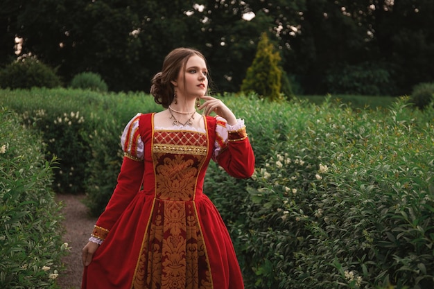 piękna młoda kobieta w czerwonej średniowiecznej sukience stoi w ogrodzie
