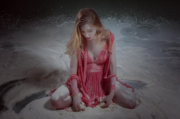 Piękna młoda kobieta w czerwonej sukience siedzi na podłodze w mące