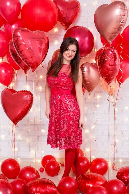 Piękna młoda kobieta w czerwonej sukience z balonami w kształcie serca