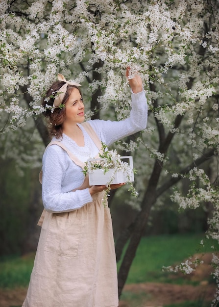 Piękna młoda kobieta w fartuchu cieszy się życiem w kwitnącym wiosną ogrodzie z kwitnącymi drzewami