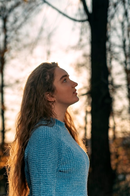 Piękna młoda kobieta w jesiennym parku o zachodzie słońca Profil dziewczyny z długimi brązowymi włosami Rama pionowa