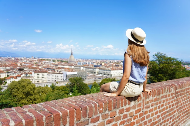 Piękna Młoda Kobieta W Kapeluszu Siedzi Na ścianie Patrząc Na Panoramę Miasta Turyn, Włochy