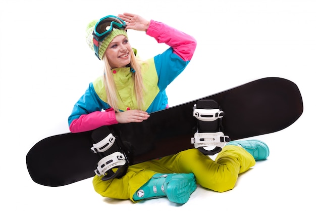 Zdjęcie piękna młoda kobieta w kombinezonie narciarskim i okularach narciarskich siedzieć z sbowboard