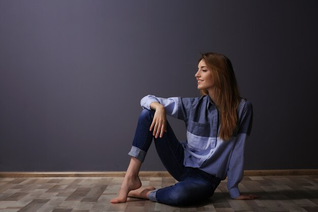 Piękna młoda kobieta w koszuli i dżinsach na szarej ścianie
