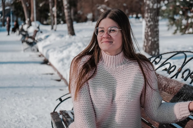 Zdjęcie piękna młoda kobieta w okularach sweter z dzianiny w winter park. zimna pogoda na zewnątrz. śnieg szczęśliwy uśmiechający się portret dziewczyny. moda zimowa