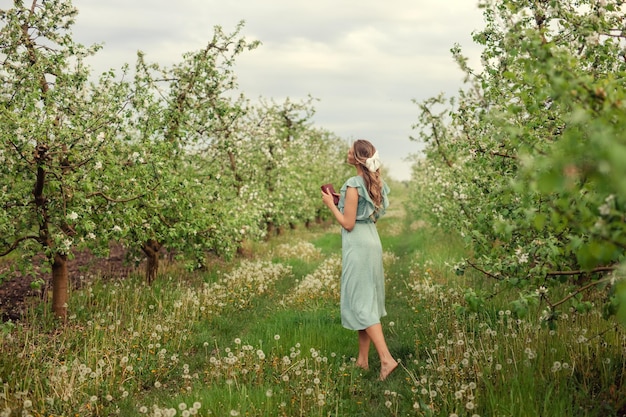 Piękna młoda kobieta w romantycznej sukience czyta wiosną drugą książkę w kwitnącym ogrodzie