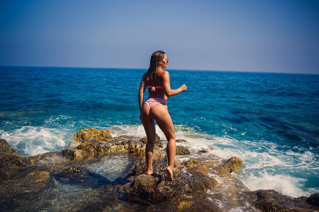 Piękna młoda kobieta w stroju kąpielowym na kamienistej plaży w słoneczny dzień na tle fal Wakacje w sezonie letnim Selektywne ustawianie ostrości