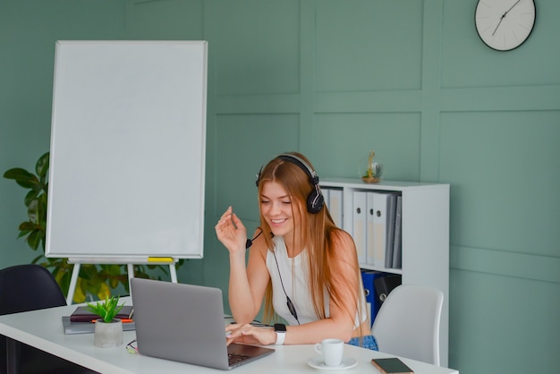 piękna młoda kobieta w zestawie słuchawkowym komunikuje się online z laptopem w biurowym stylu życia f