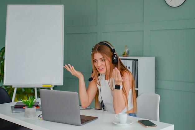 piękna młoda kobieta w zestawie słuchawkowym komunikuje się online z laptopem w biurowym stylu życia f