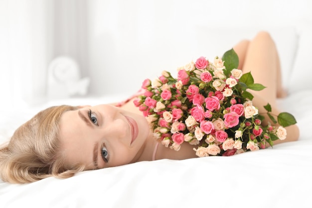 Piękna młoda kobieta z bukietem róż na łóżku w domu
