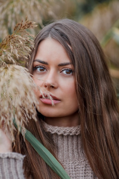 Piękna młoda kobieta z długimi włosami i brązowymi oczami w jesiennym parku Portret modelki w swetrze z dzianiny w pobliżu trawy pampasowej