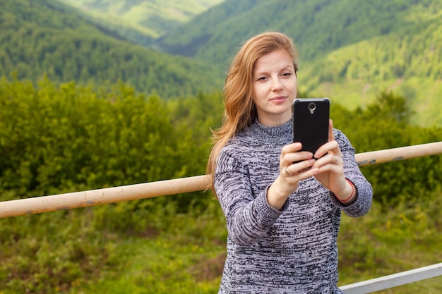 Piękna młoda kobieta z długimi włosami robi selfie na swoim telefonie na tle zielonej natury