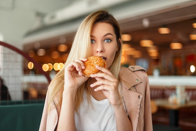 Piękna młoda kobieta z hamburgerem w restauracji