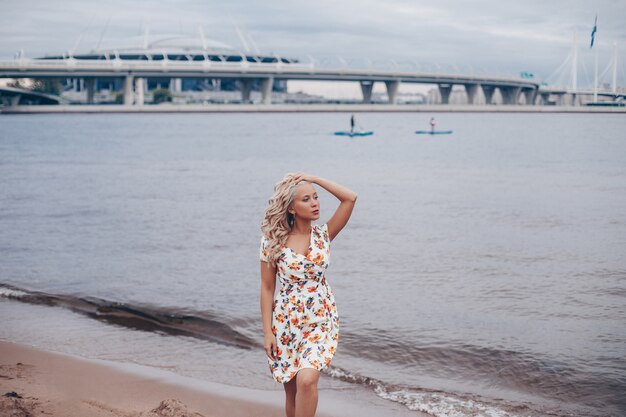 Piękna młoda kobieta z kręconymi blond włosami, w letniej sukience spaceru w pobliżu morza