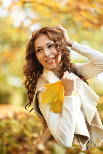 Piękna młoda kobieta z liśćmi pozuje w jesiennym parku