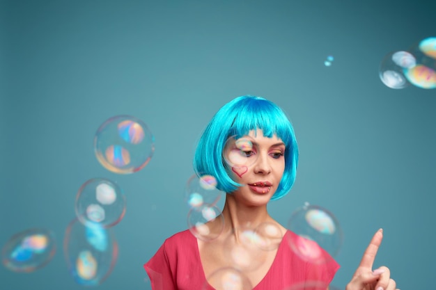 Piękna młoda kobieta z niebieską peruką i jasnym makijażem w bańkach mydlanych Modelka dziewczyna z kreatywnym kolorowym makijażem Koncepcja lalek dla kobiet
