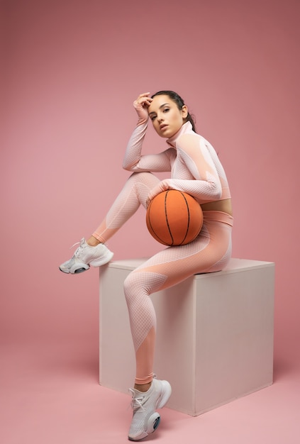 Piękna młoda kobieta z piłką do koszykówki siedzącą na sześcianie